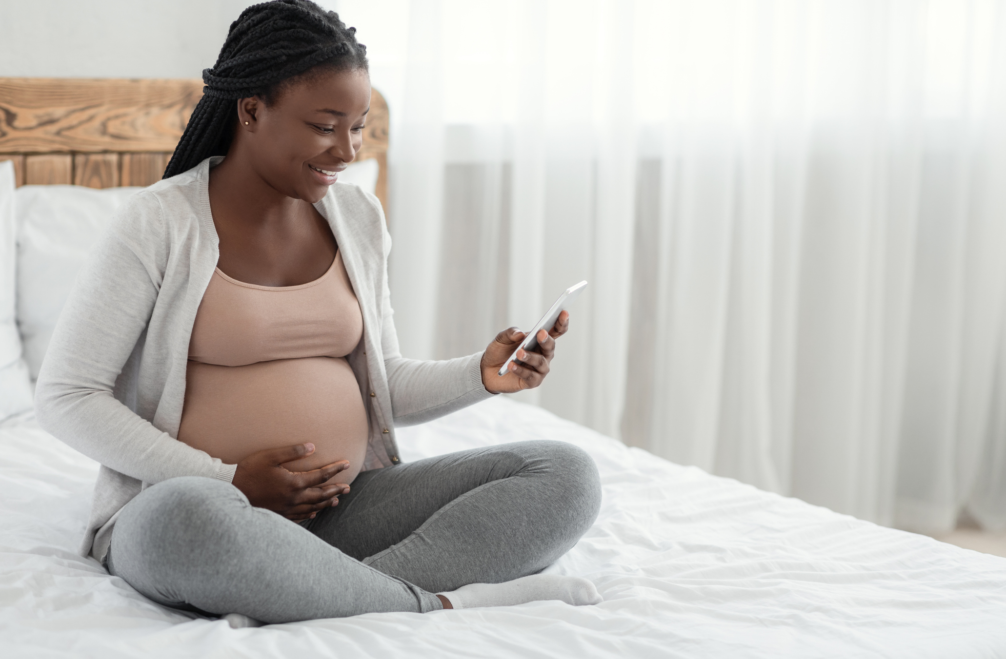 Excited Black Pregnant Woman Sitting With Smartphone On Bed At Home stock photo