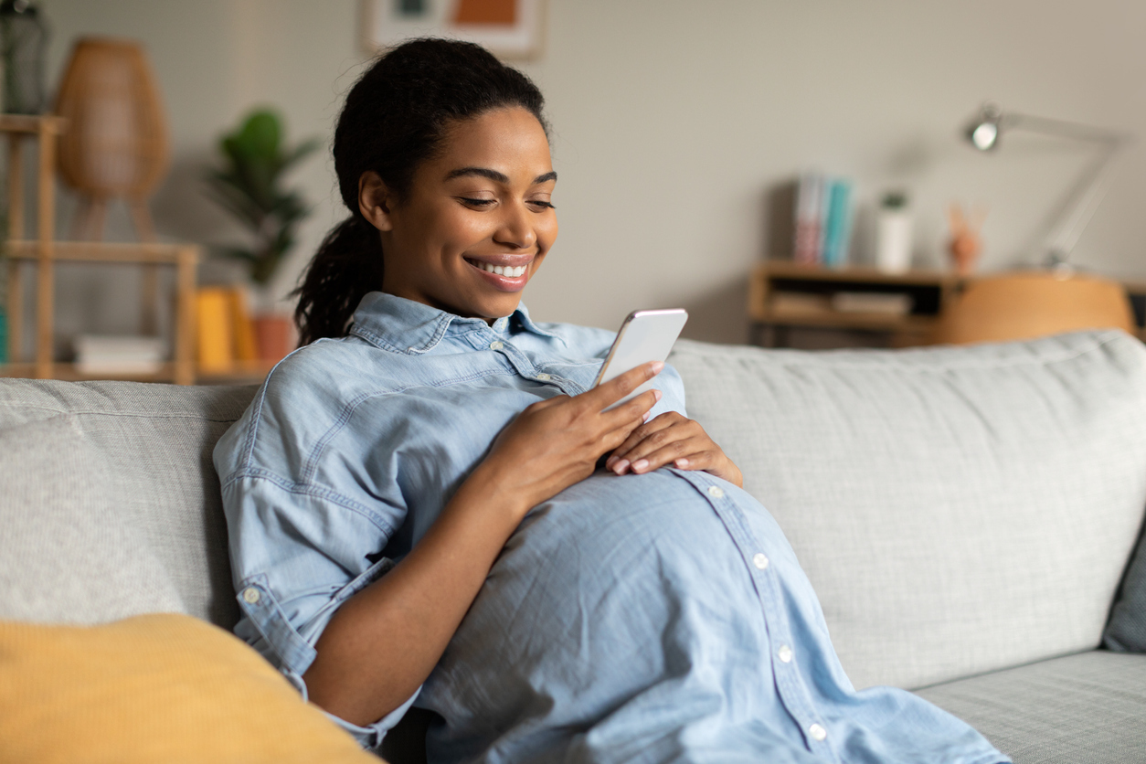 A pregnant woman smiling while looking at her phone, possibly researching Medela Breast Pumps. This image reflects the excitement and preparation for motherhood, including choosing the right breast pump.