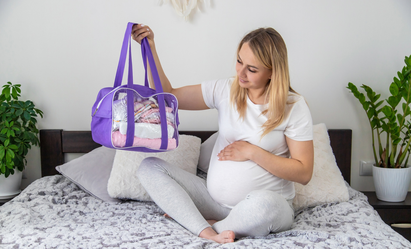 A pregnant woman collects baby things in a purple tote as she begins her hospital bag packing