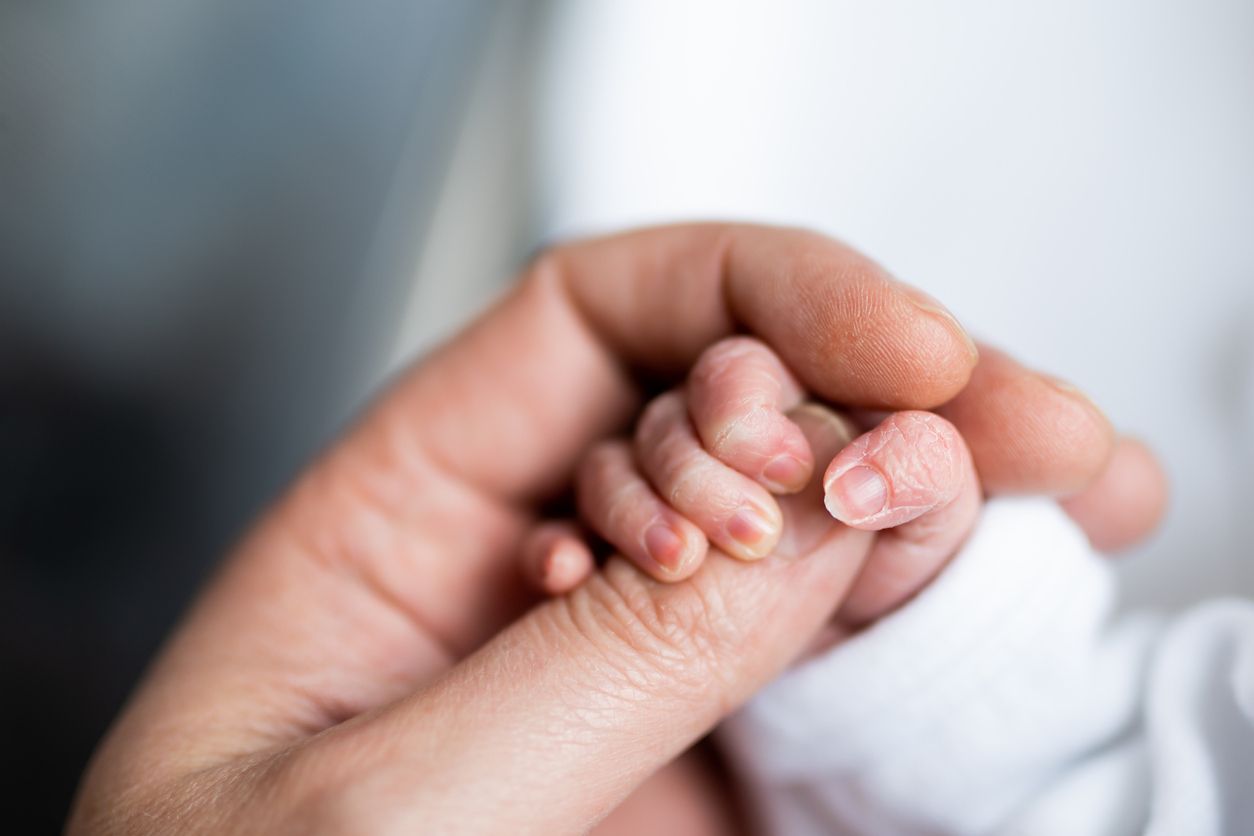 Close-up of a newborn's tiny hand gently holding an adult's finger, symbolizing love and support. This image reflects tips for preemie moms on providing comfort, care, and nurturing to their little ones.