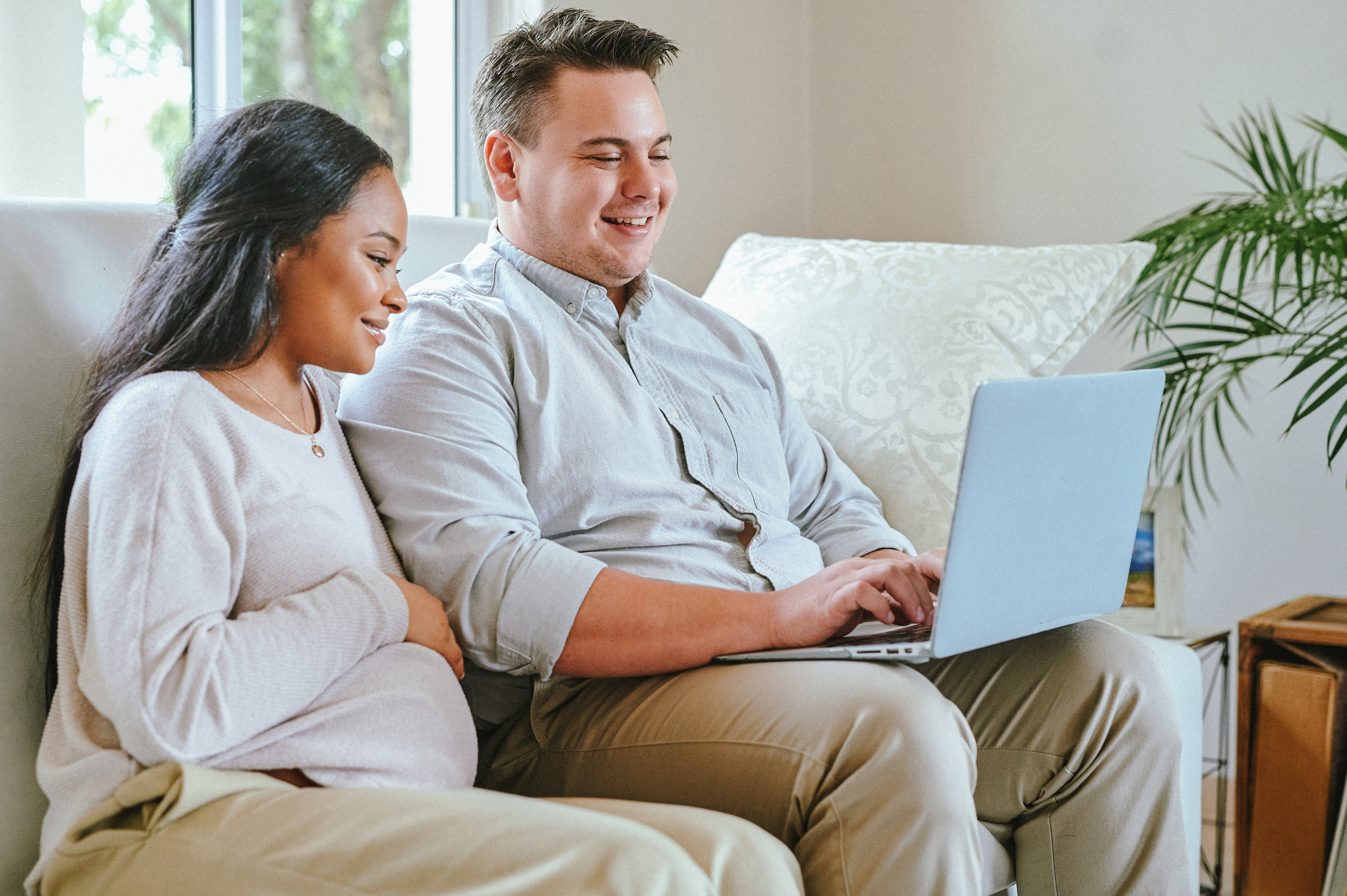 Pregnant woman and her husband on a couch looking at their laptop looking for a Free Breast Pump Through Insurance