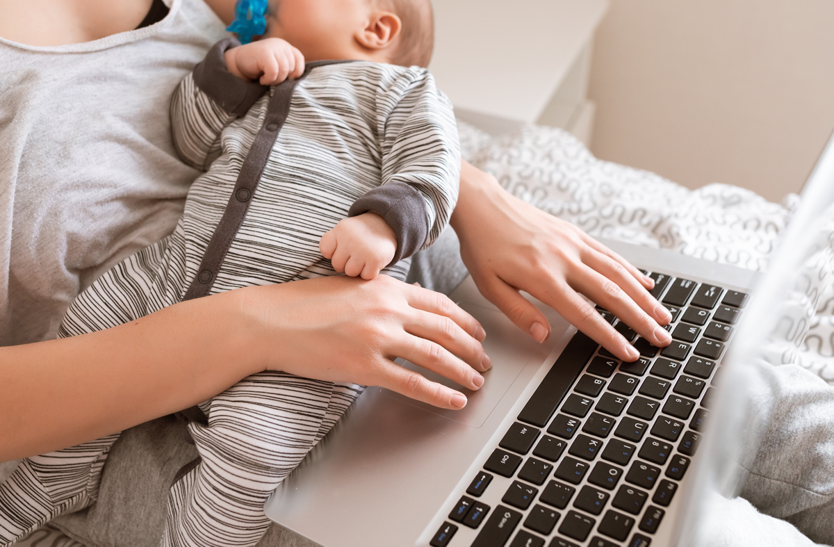 Mother working on a laptop while holding her baby, illustrating multitasking and the convenience of hands-free pumping technology for busy parents.