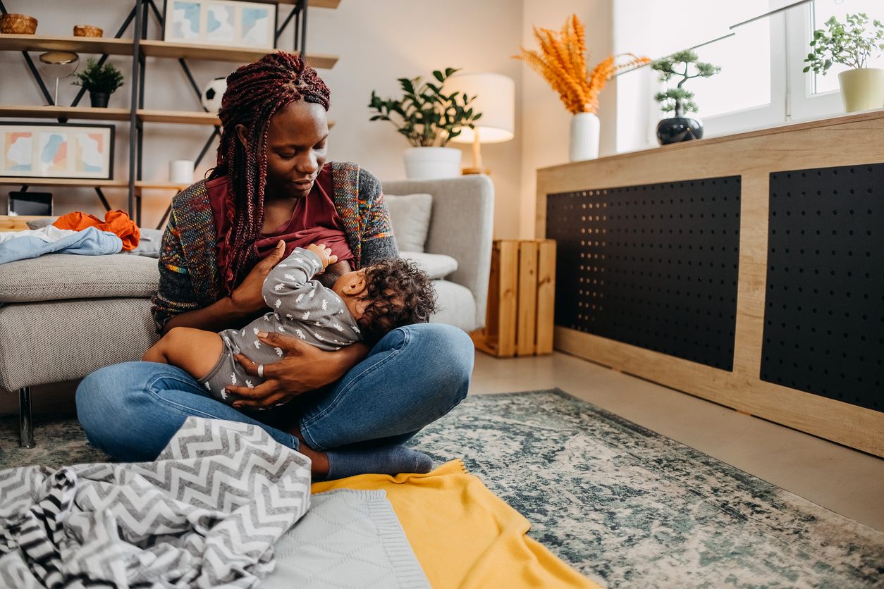 woman in living room sitting on the floor with her baby reflecting on the perks of getting a breast pump