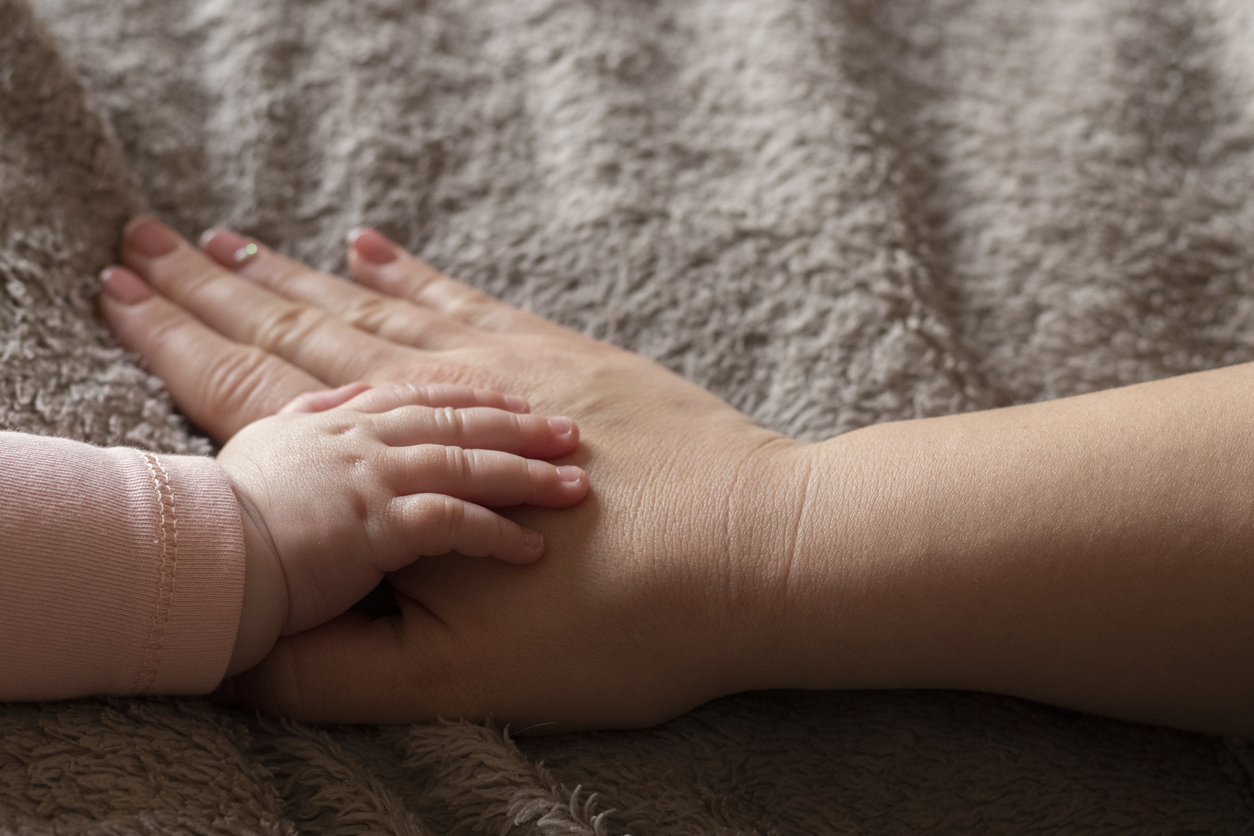 Baby's hand resting on woman's hand -- which is resting on her swollen stomach, a result of postpartum edema