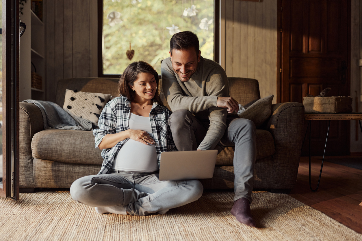 Happy pregnant woman in the living room with her husband looking at the computer showing him the Pumps for Mom ordering process.