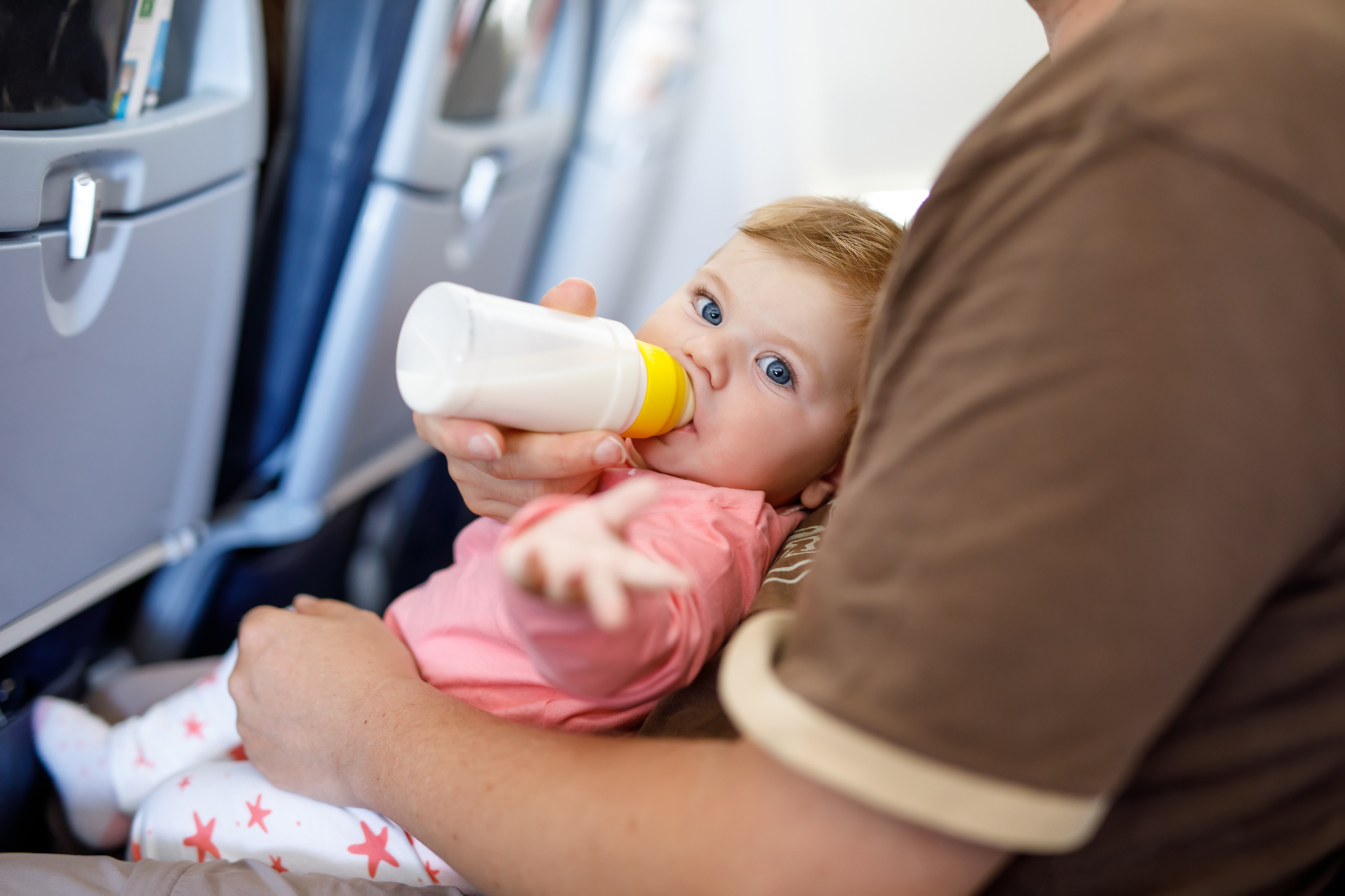 A baby being bottle-fed while sitting on a caregiver's lap during a flight, illustrating the convenience of traveling while breast pumping. This image highlights how pumped milk can make feeding easier when on the go.